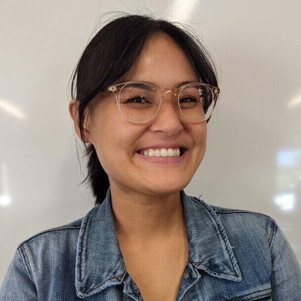 Smiling woman in denim jacket and glasses.
