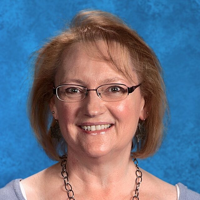 Smiling woman with glasses and necklace.
